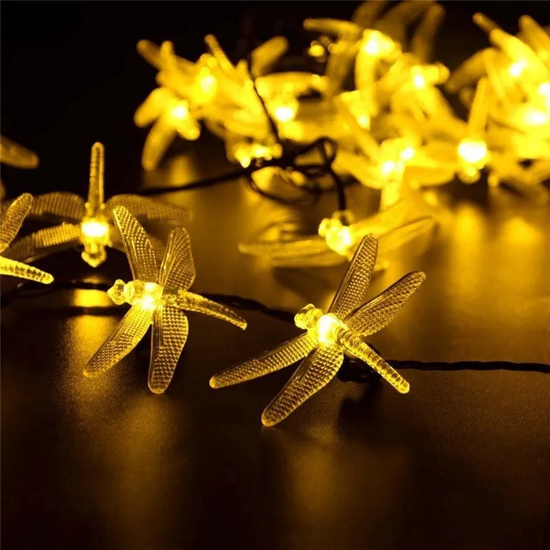 Outdoor solar-powered dragonfly LED string lights with panel on spike in a garden setting
