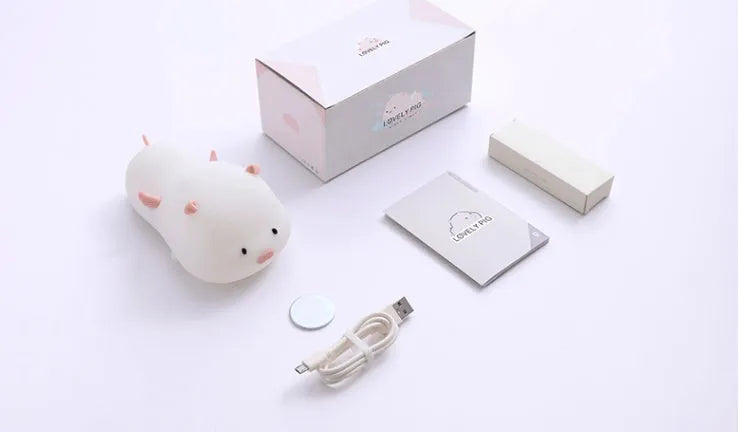 Blue rechargeable pig-shaped silicone night light with a sleeping design on a bedside table.
