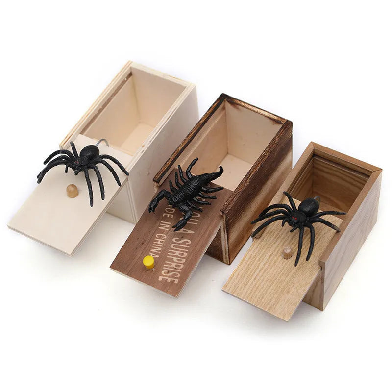 Wooden prank box with lid open showing a lifelike jumping spider inside on a white background.