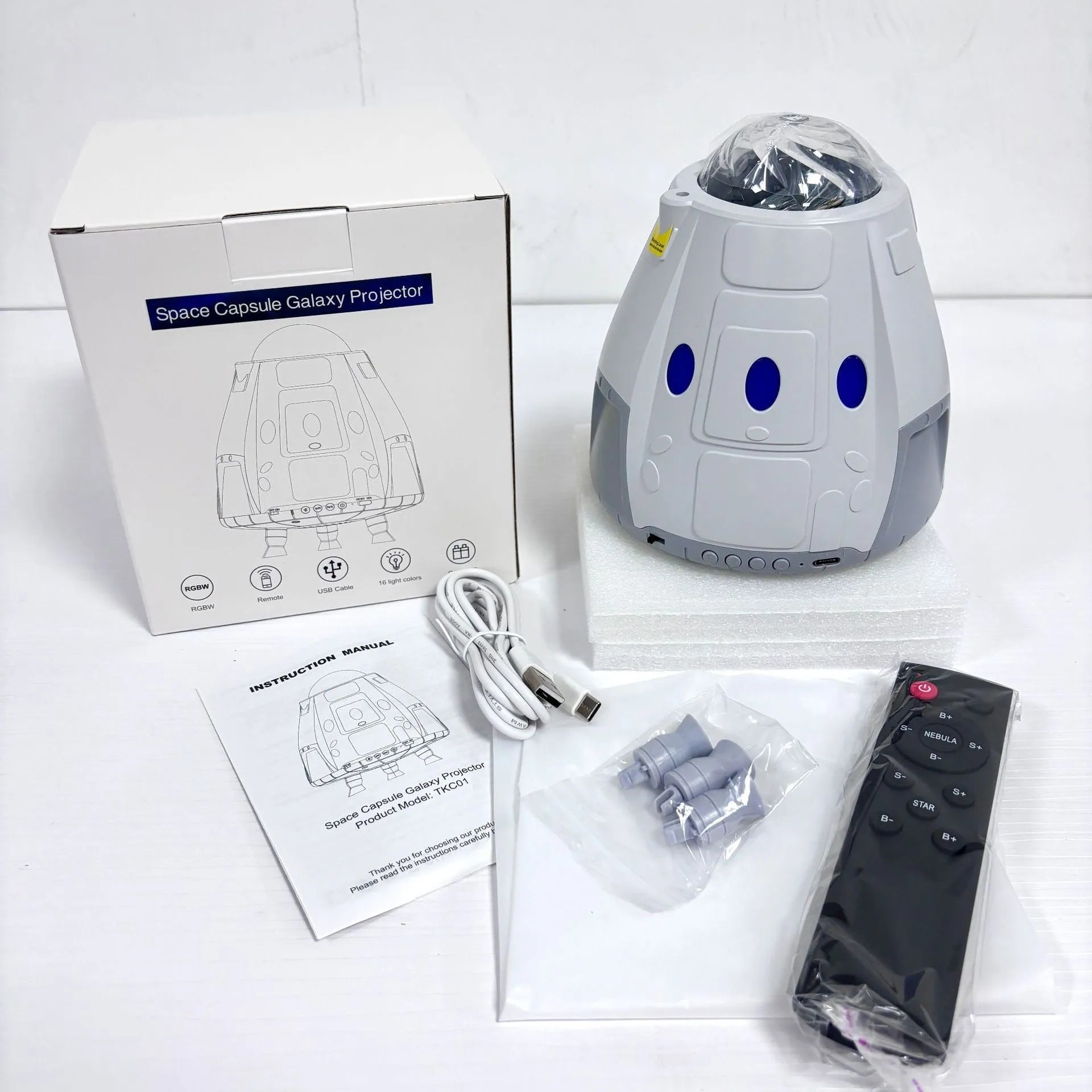 Space Capsule USB Galaxy Projection Lamp in white or grey with remote control on a table.