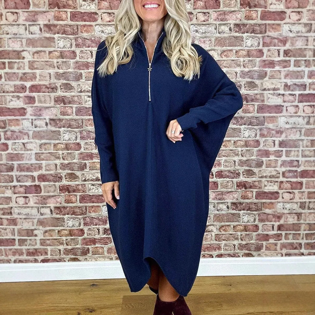 A woman wearing a solid dark green loose-fit knitted dress with raglan sleeves and a zipper detail.