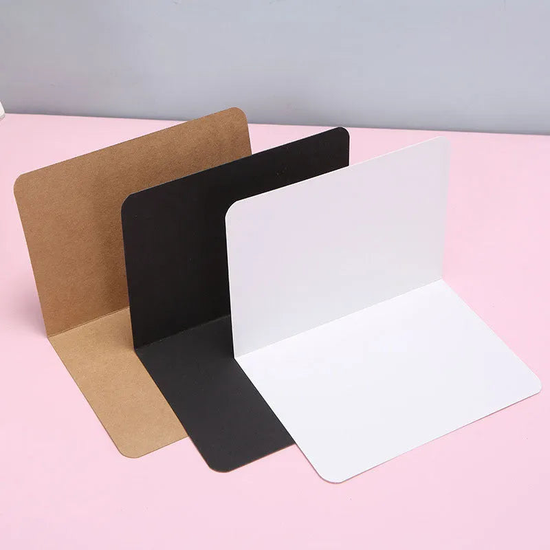 Pack of 100 blank folded kraft paper cards in 10x15 cm size, shown in black, brown, and white colours.