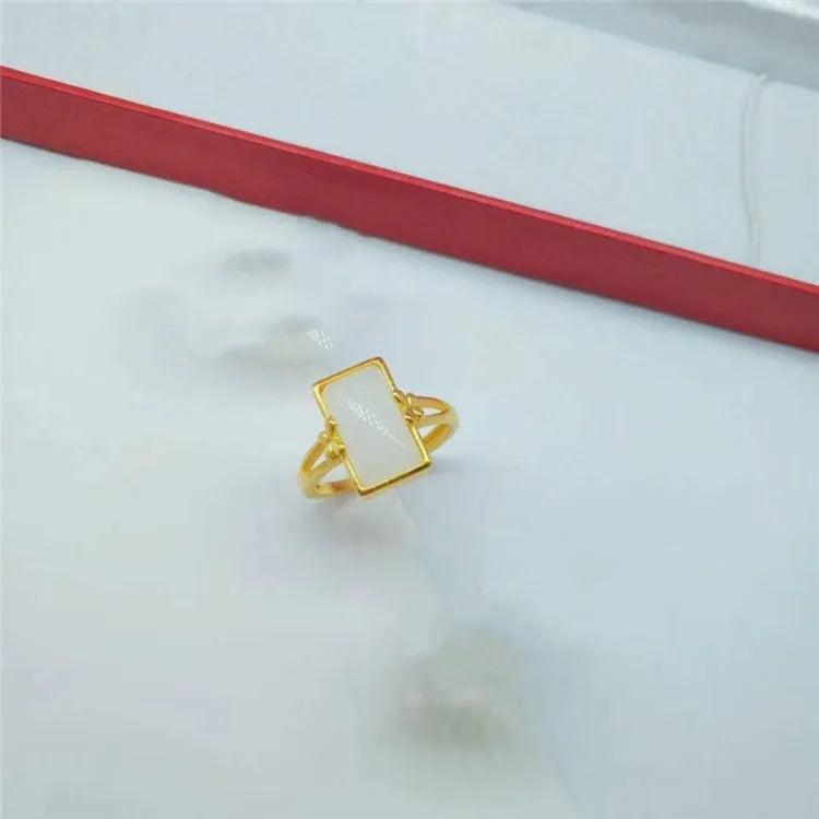 Adjustable brass gold-plated ring with a central green gemstone inlay on a finger.