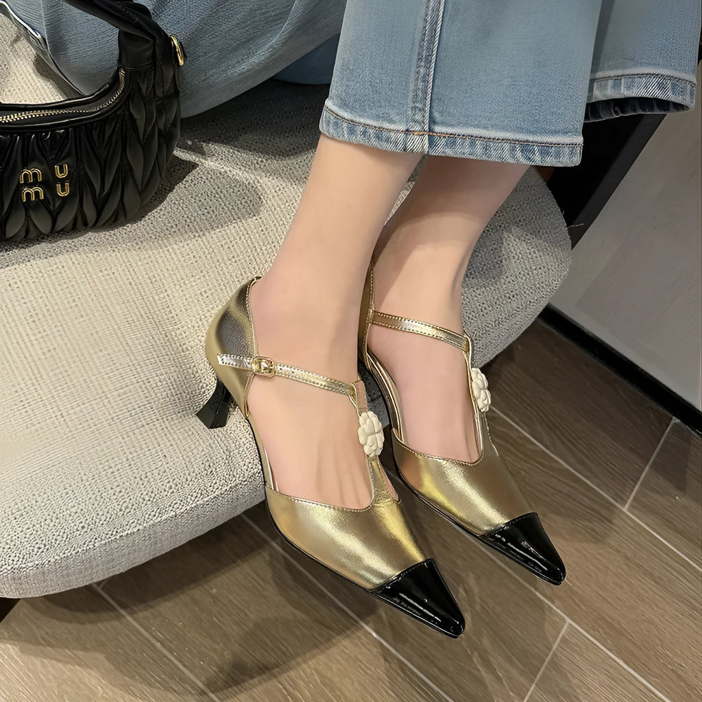 Gold women's stiletto heel shoe with flower buckle and pointed toe on a white background.