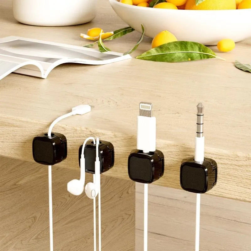 White and black magnetic cable clips with adhesive backing organising multiple cables under a desk