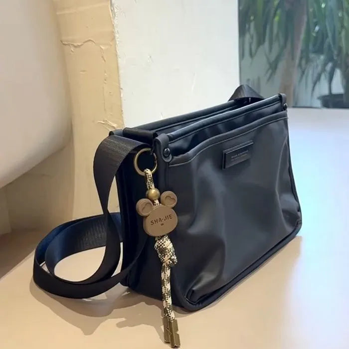 Small square crossbody bag in Oxford cloth, shown in a solid colour on an adjustable strap.