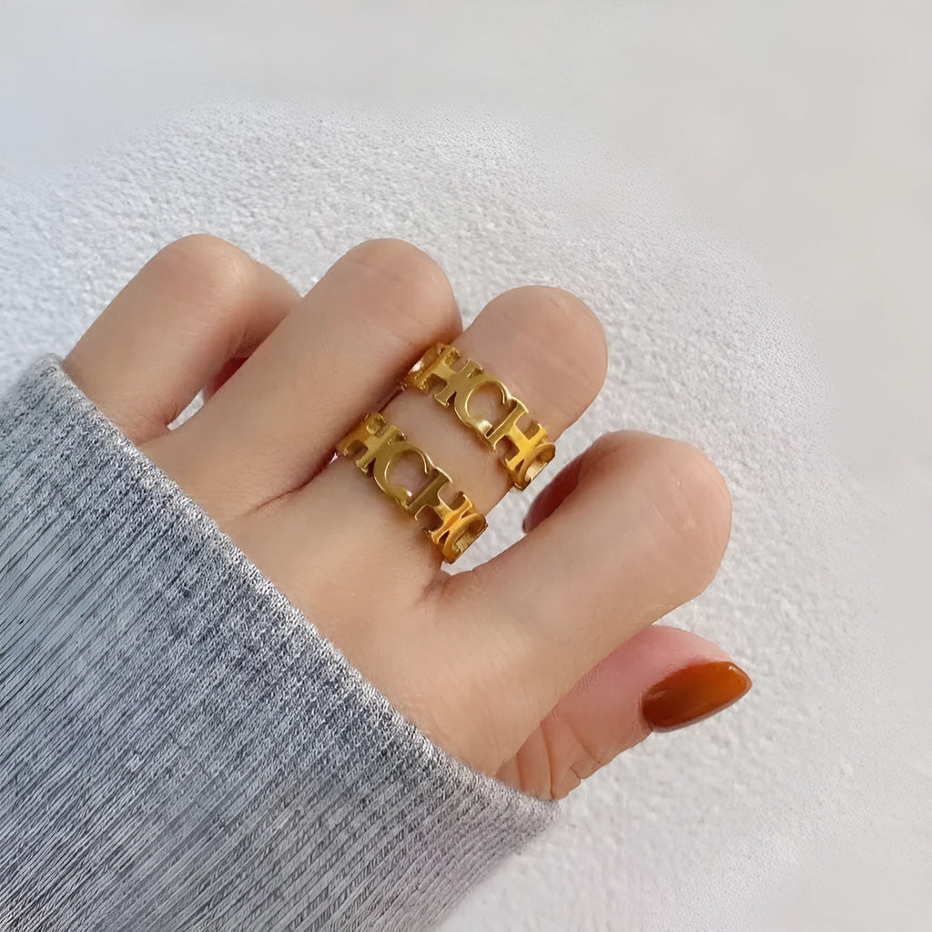 Gold titanium steel hollowed cut letter ring with geometric design on white background