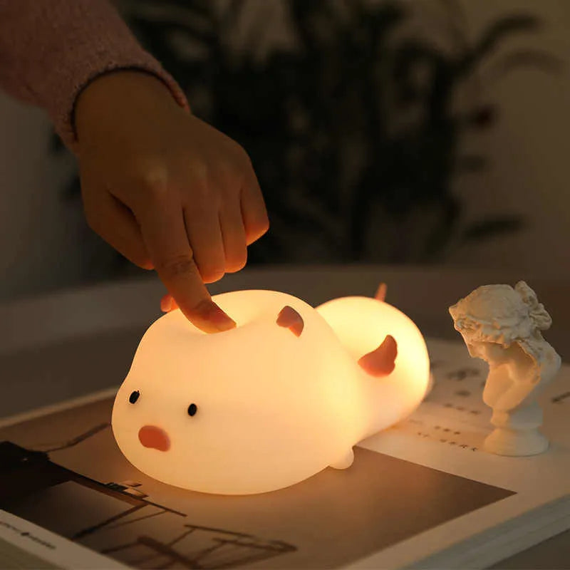 Blue rechargeable pig-shaped silicone night light with a sleeping design on a bedside table.