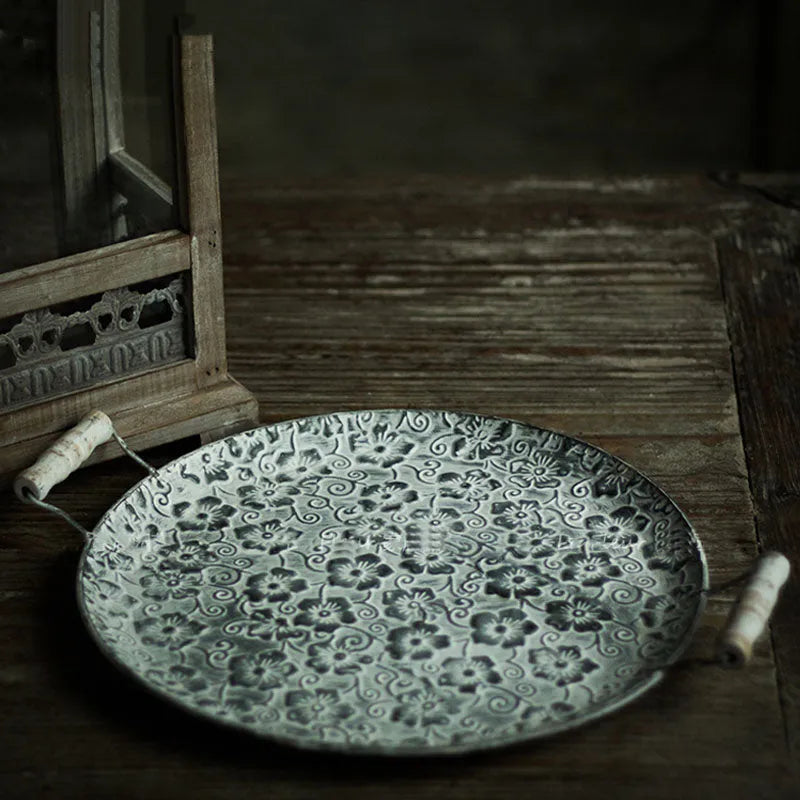 Round wrought iron belt storage tray with raised rim in two sizes on a wooden table.