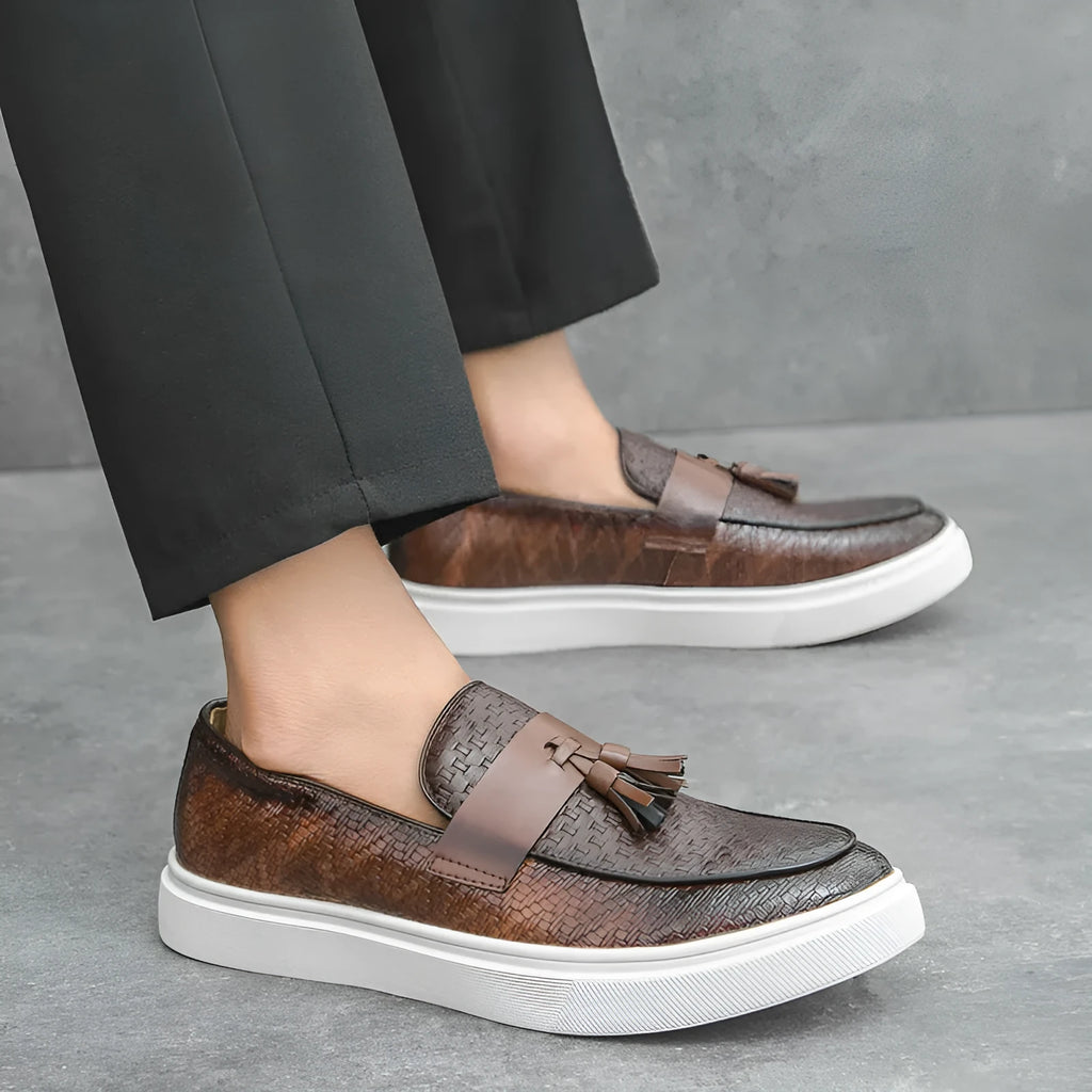 Men's black casual leather shoes with fringe detail on round toe, showing low heel profile.