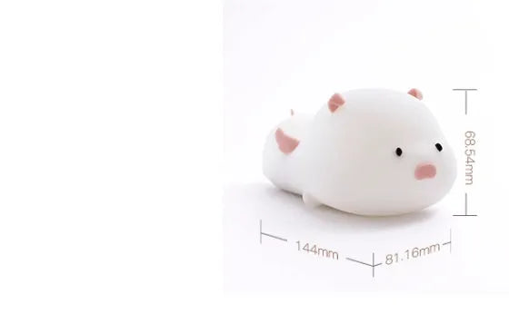 Blue rechargeable pig-shaped silicone night light with a sleeping design on a bedside table.
