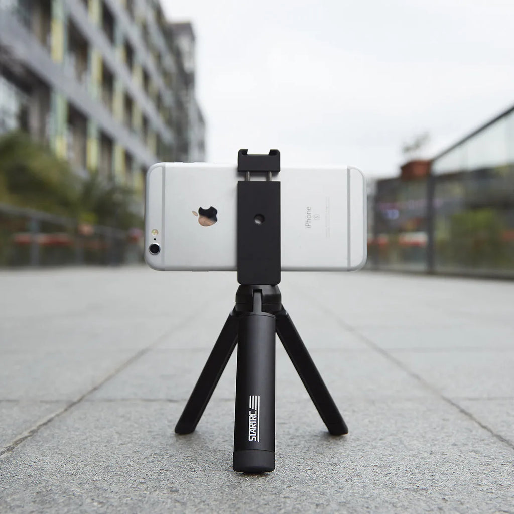 Silver aluminium smartphone bracket for tripod mounting next to a mobile phone.