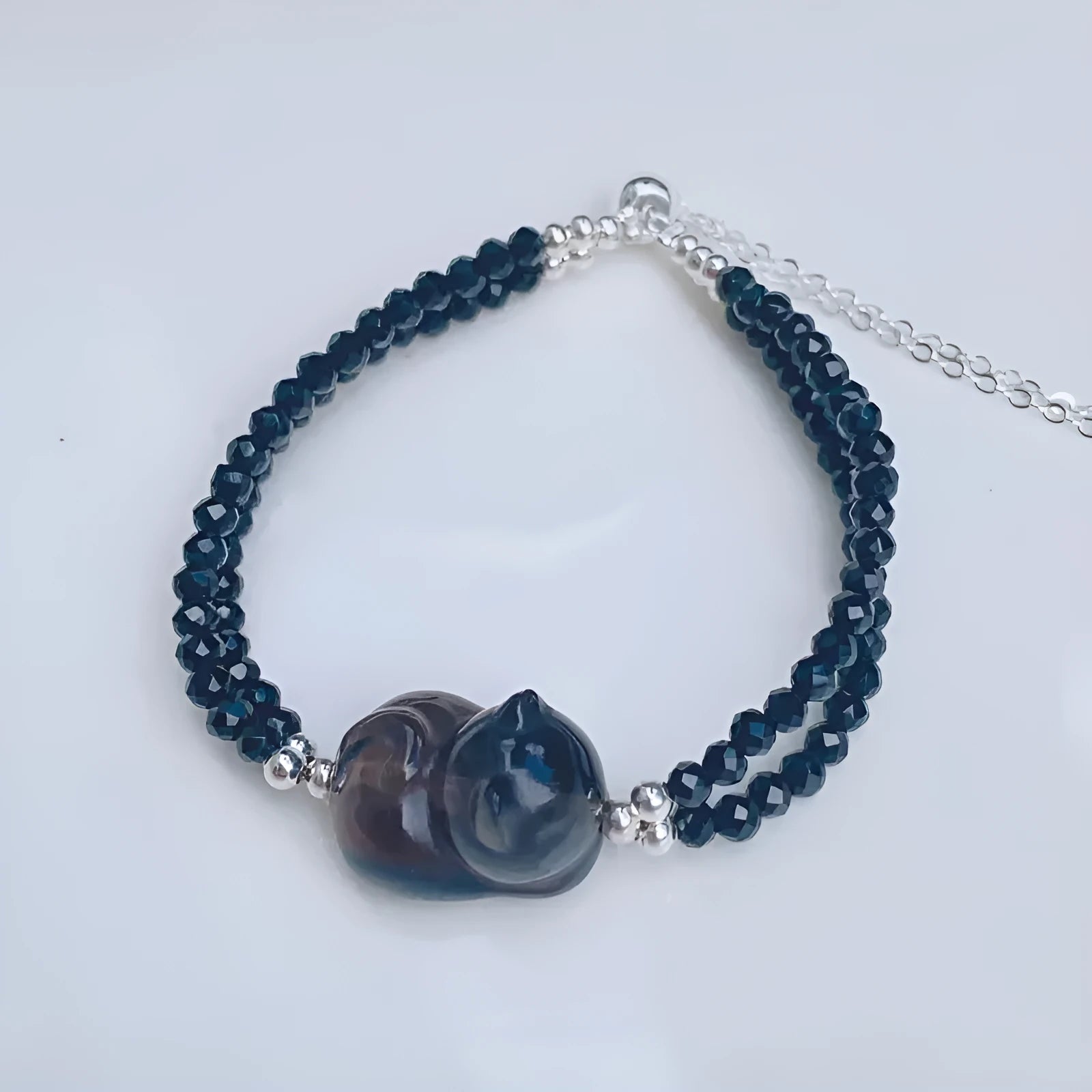 Obsidian bracelet with a hand-carved climbing cat charm on a dark background.