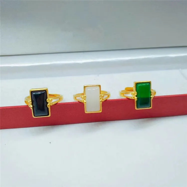 Adjustable brass gold-plated ring with a central green gemstone inlay on a finger.
