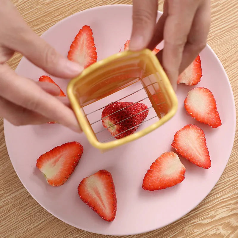 Green stainless steel cup fruit slicer with sliced strawberries on a light background