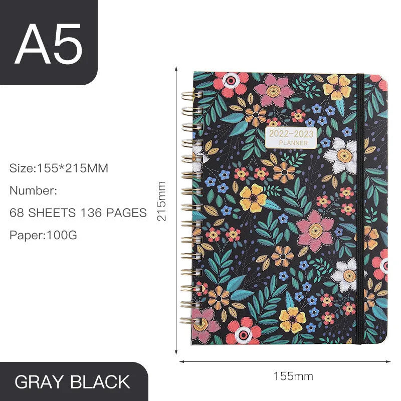 A5 spiral-bound notebook with a colourful floral design cover, lying open on a table.