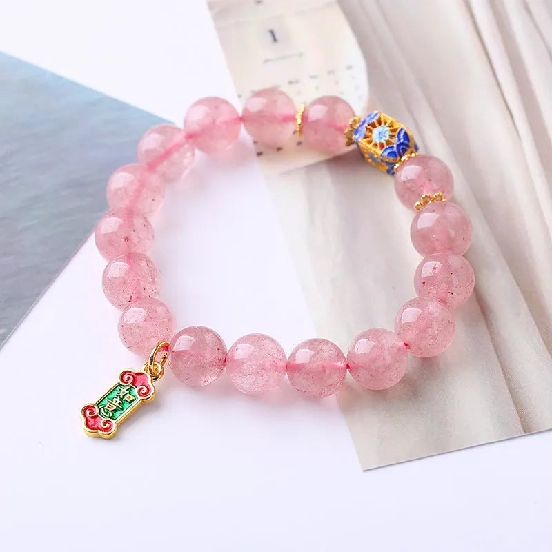 Close-up of a pink Strawberry Quartz crystal bracelet with hand-woven beads and a golden Ruyi symbol charm.