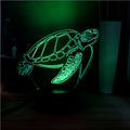3D clear acrylic turtle-shaped LED night light with remote control on a desk.