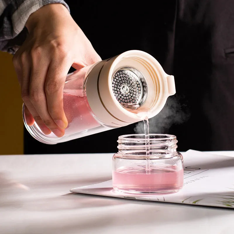 Green double-wall glass water bottle with tea infuser, stainless steel filter, and rope handle on a wooden table.