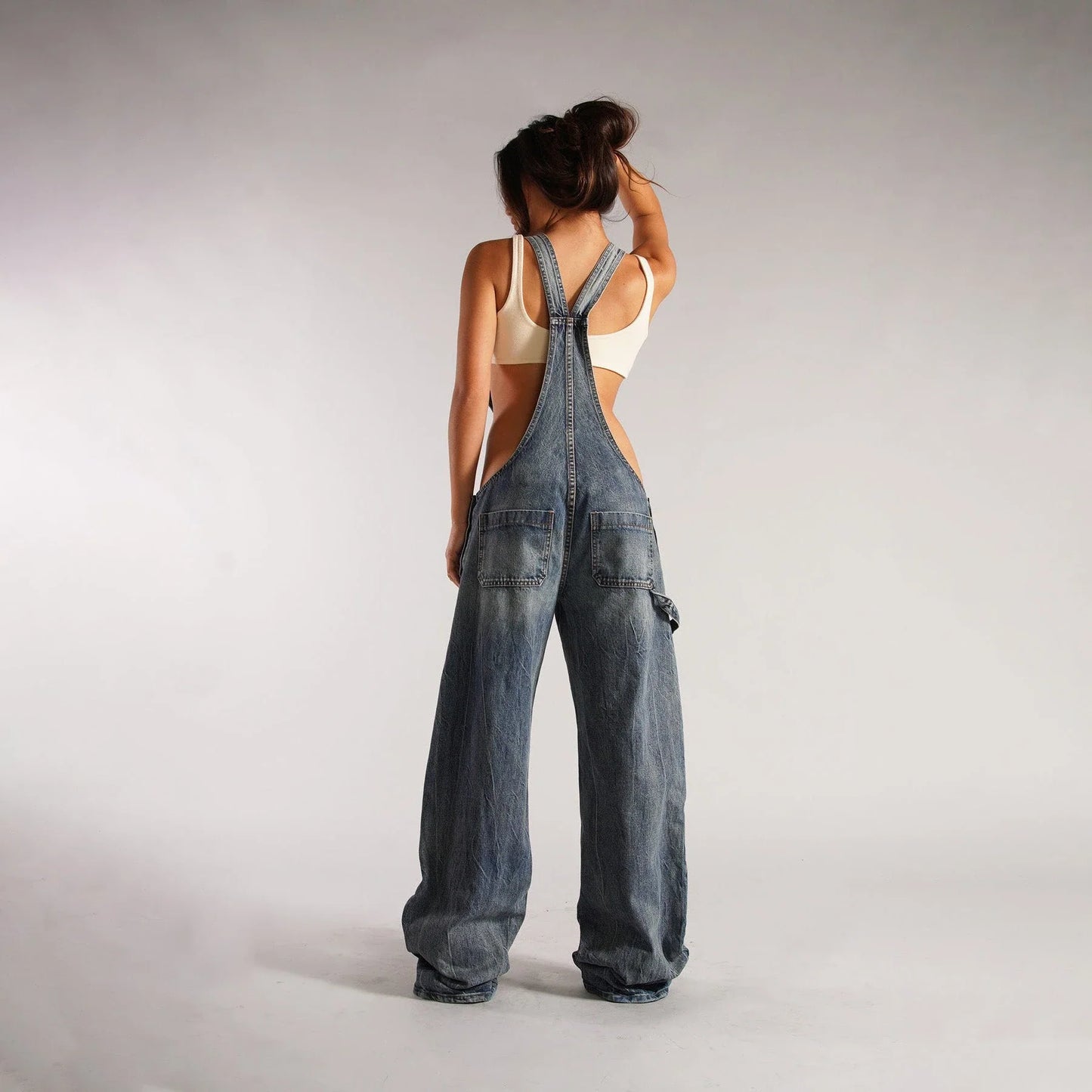 Stylish Y2K-inspired denim suspender jumpsuit with pockets, featuring a relaxed wide-leg silhouette and adjustable straps for a customized fit.