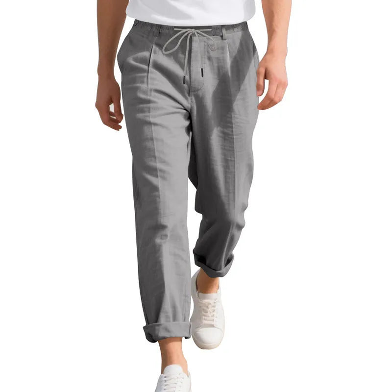 Men's light beige linen trousers with drawstring waist and straight-leg design laid flat