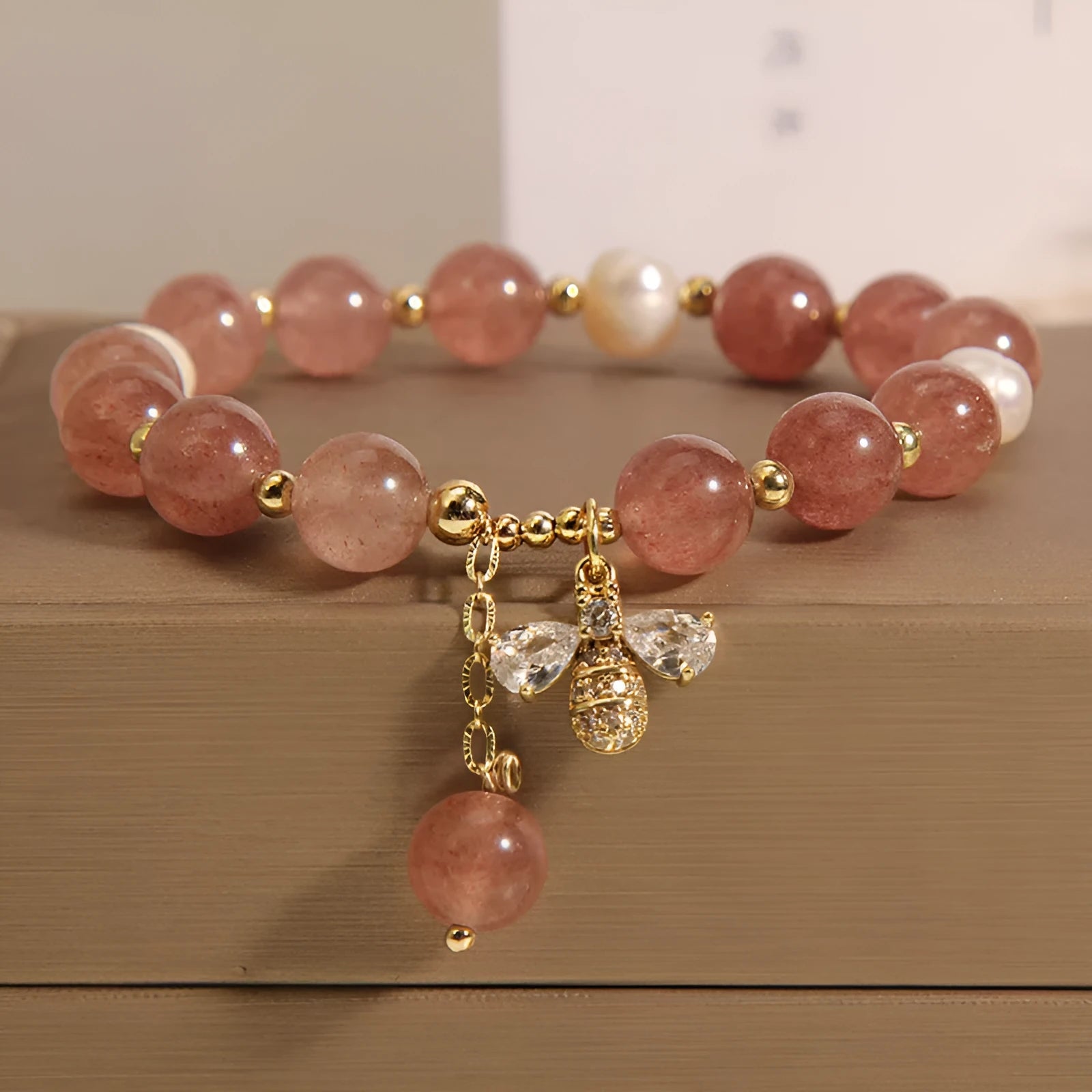 Close-up of a women's bracelet with strawberry quartz, freshwater pearls, a bee charm, and zircon accents on an alloy chain.