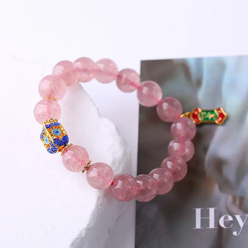 Close-up of a pink Strawberry Quartz crystal bracelet with hand-woven beads and a golden Ruyi symbol charm.