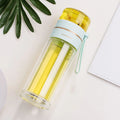 Green double-wall glass water bottle with tea infuser, stainless steel filter, and rope handle on a wooden table.