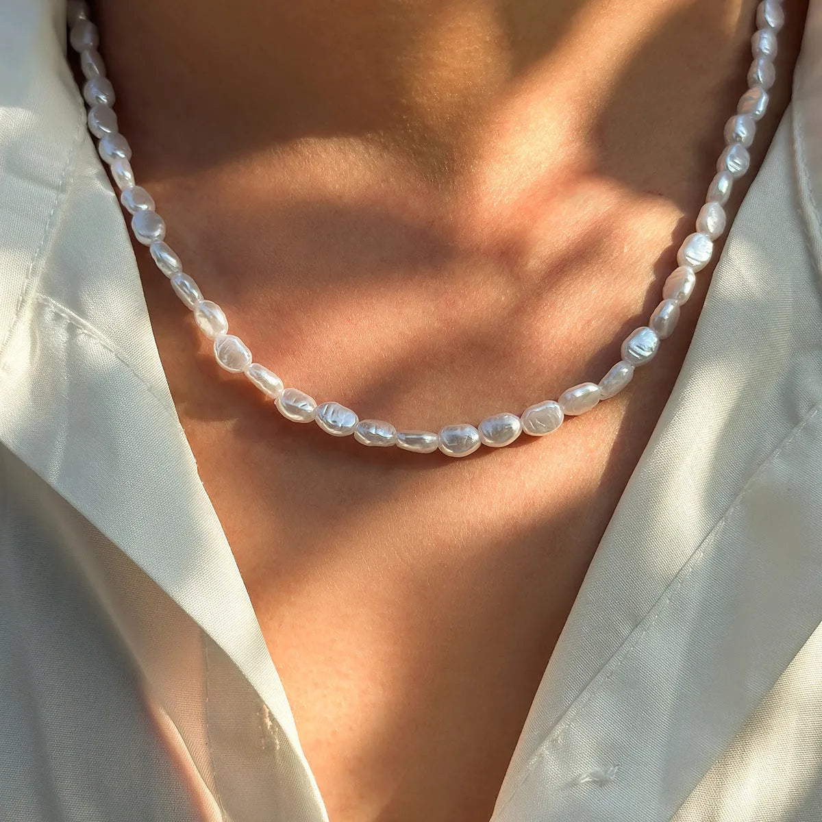 White U-shaped imitation pearl men's necklace with a shellfish pendant on a model.