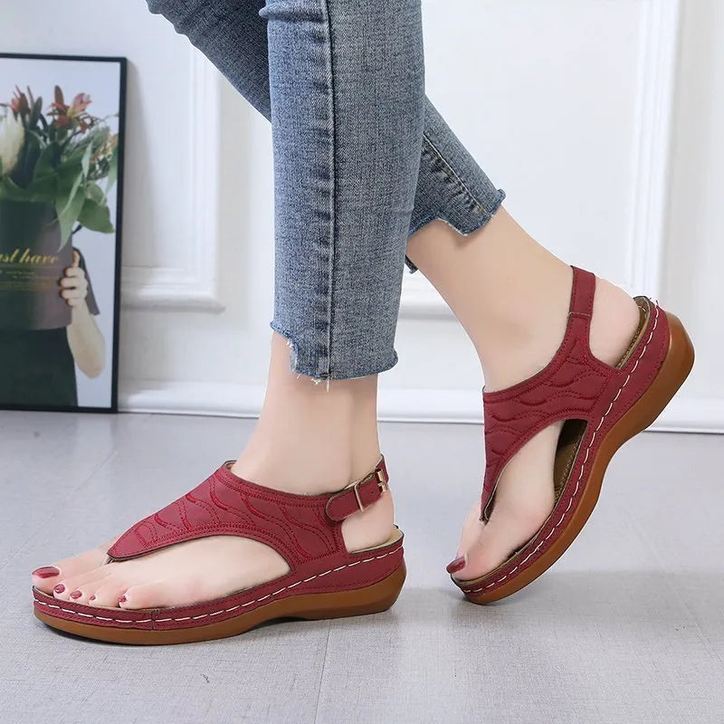 Women's beige wedge heel flip flop sandals with an adjustable buckle strap on a wooden deck.