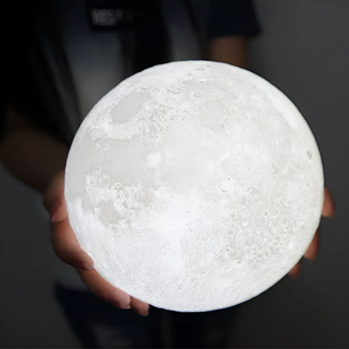 3D printed white moon lamp glowing on a wooden stand, showing detailed lunar craters.