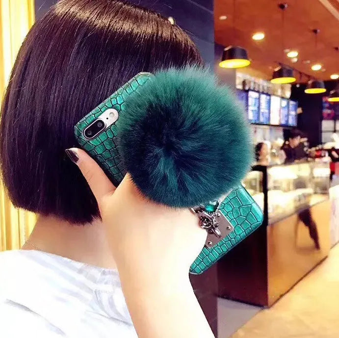 Red PU leather iPhone case with rhinestone studs and a white fox fur ball charm attached.