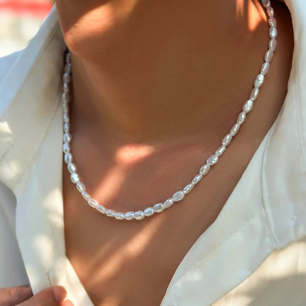 White U-shaped imitation pearl men's necklace with a shellfish pendant on a model.