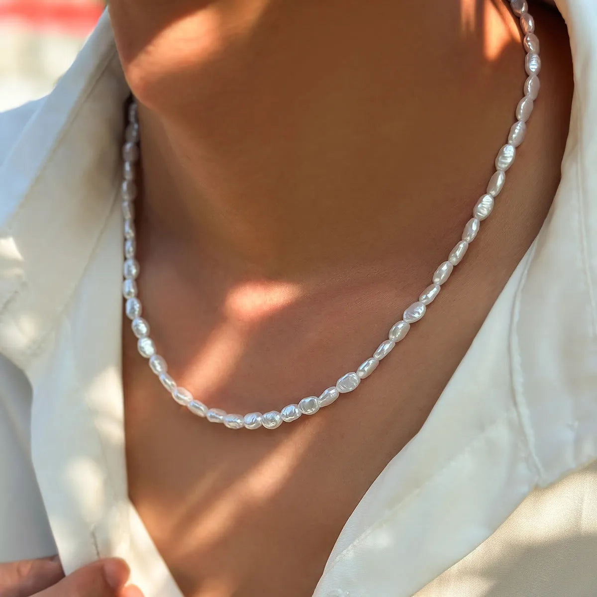 White U-shaped imitation pearl men's necklace with a shellfish pendant on a model.