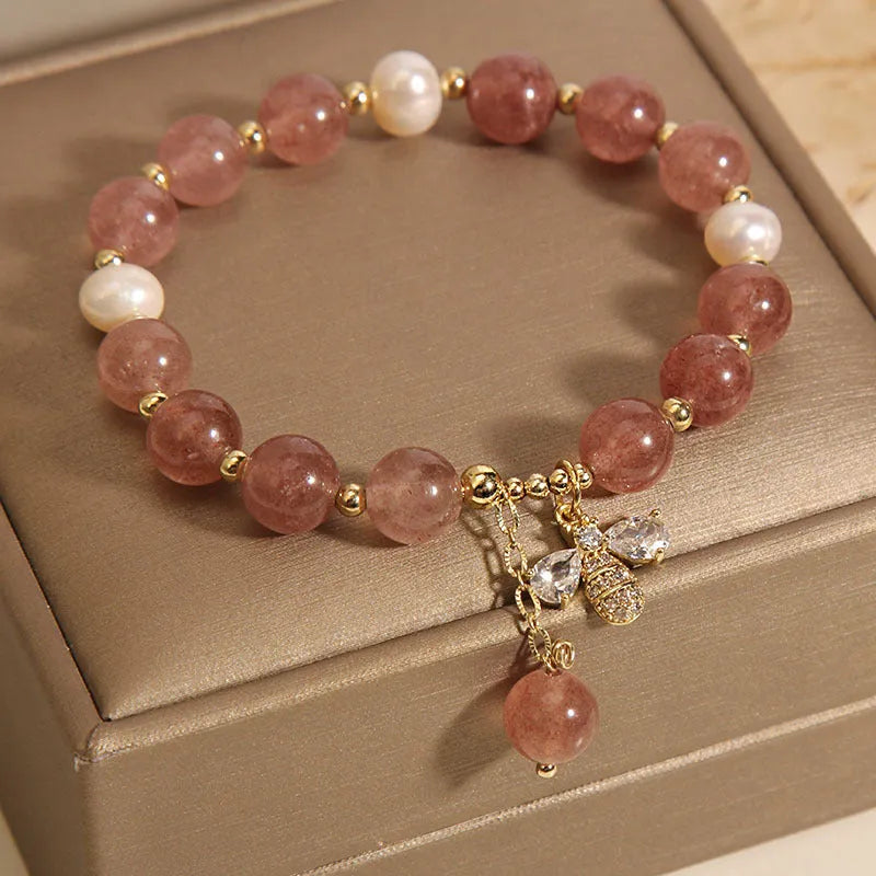 Close-up of a women's bracelet with strawberry quartz, freshwater pearls, a bee charm, and zircon accents on an alloy chain.