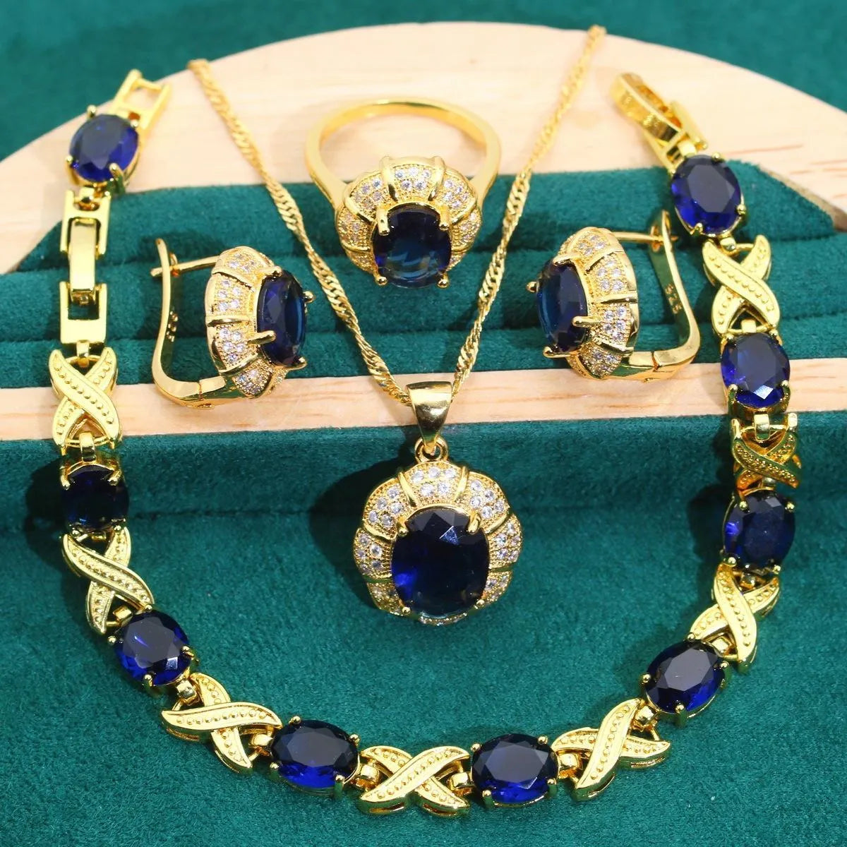 Gold-coloured jewellery set with sparkling blue cubic zirconia stones, showing necklace, earrings, ring, and bracelet.