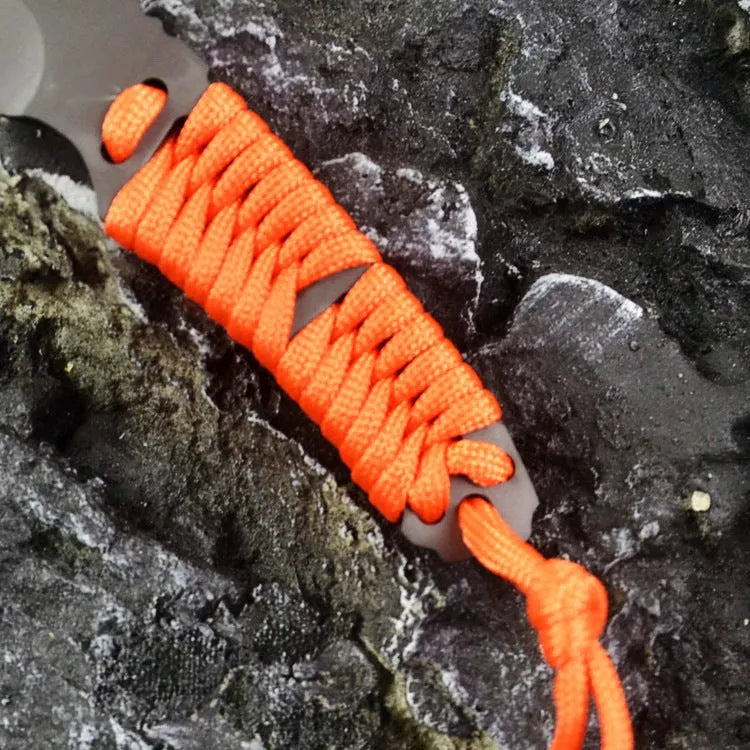 Straight blade outdoor survival knife with binding rope handle next to ABS plastic sheath