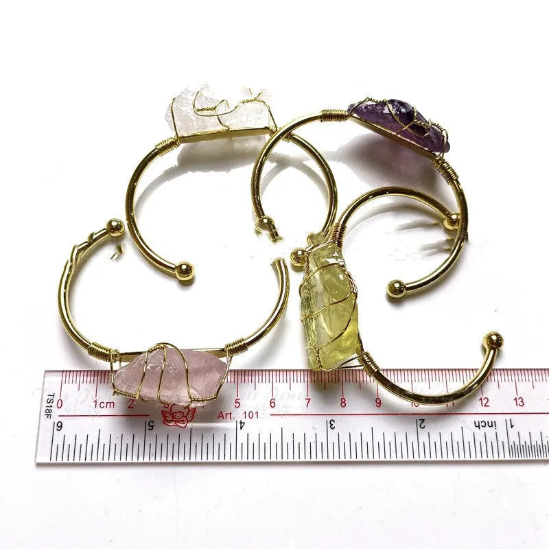 Rough natural crystal bracelet with gold winding geometric design on a wrist.