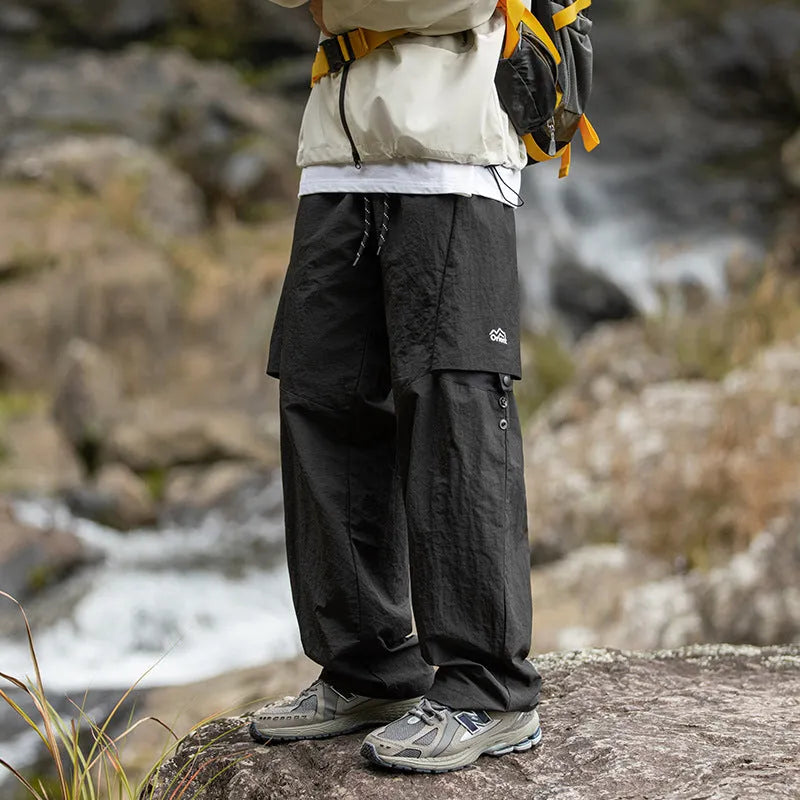 Men's loose-fit nylon casual trousers in black, grey green, or greige, with adjustable split and breathable fabric.