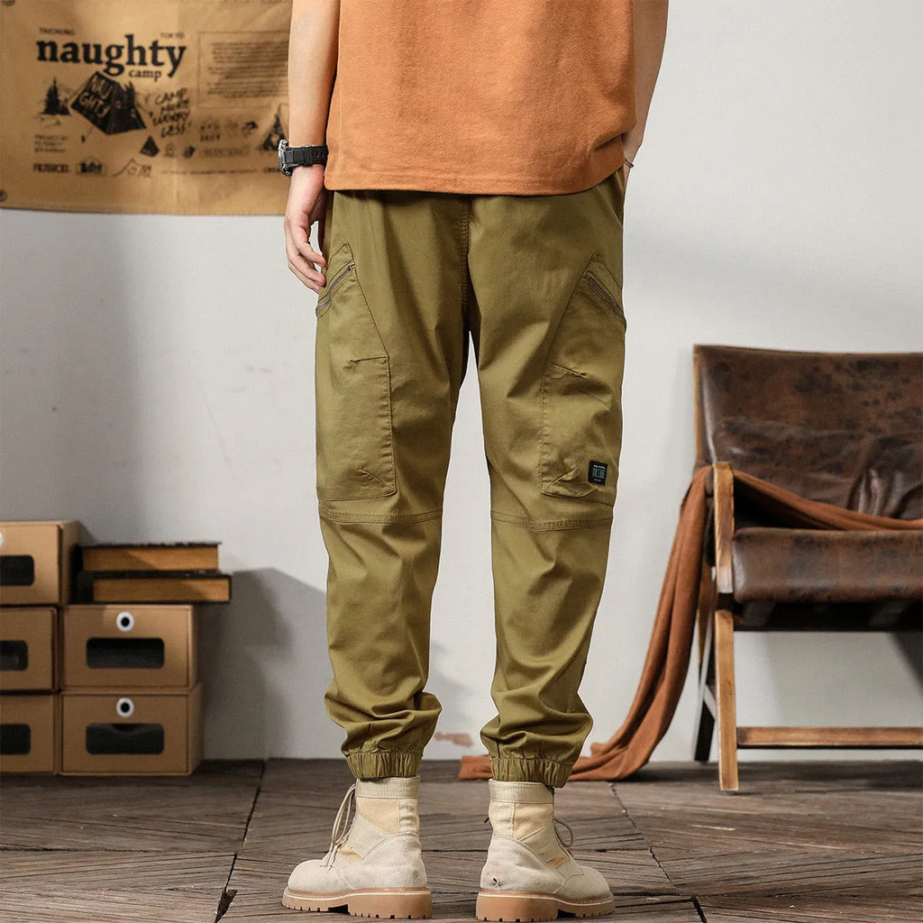 Men's khaki cotton harem pants with tapered ankle cuffs and a loose fit, shown laid flat.
