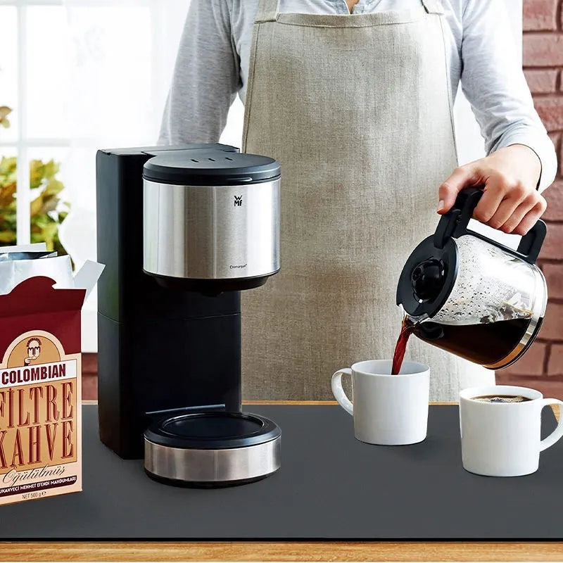 Black square rubber-backed kitchen drying mat on a countertop next to a coffee cup