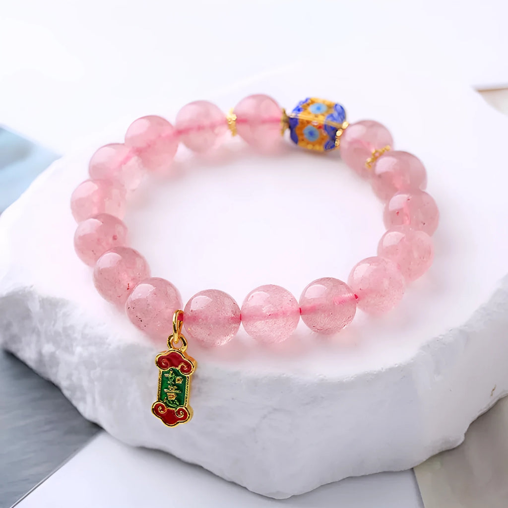 Close-up of a pink Strawberry Quartz crystal bracelet with hand-woven beads and a golden Ruyi symbol charm.
