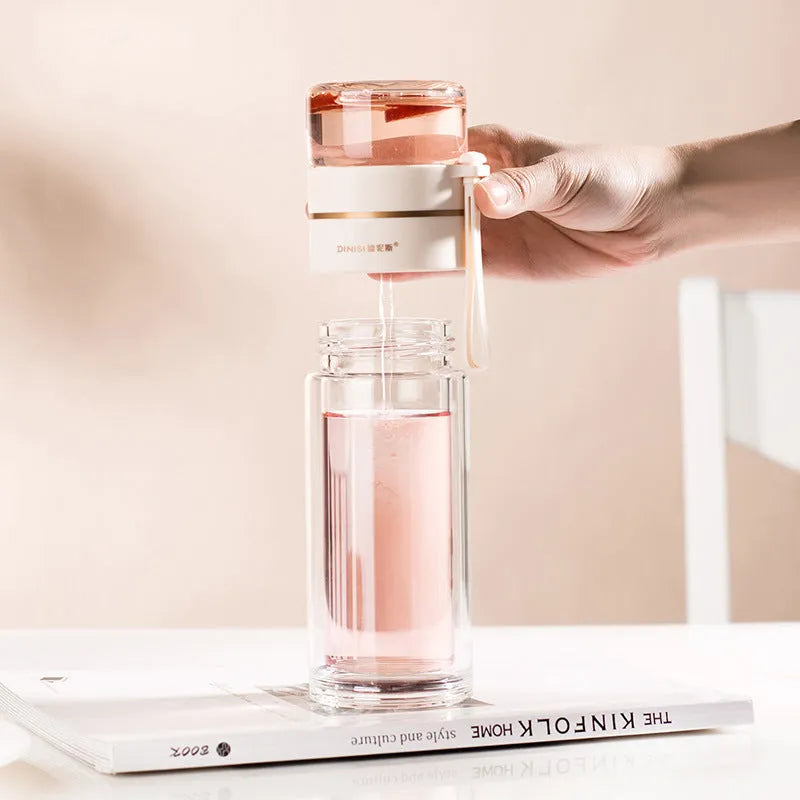 Green double-wall glass water bottle with tea infuser, stainless steel filter, and rope handle on a wooden table.