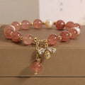 Close-up of a women's bracelet with strawberry quartz, freshwater pearls, a bee charm, and zircon accents on an alloy chain.