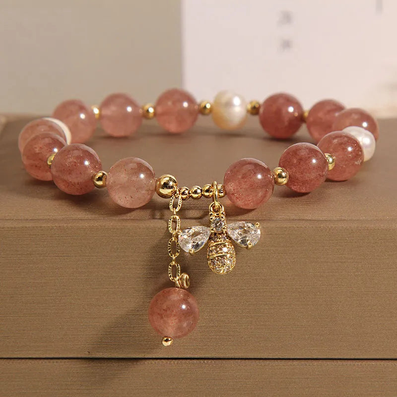 Close-up of a women's bracelet with strawberry quartz, freshwater pearls, a bee charm, and zircon accents on an alloy chain.