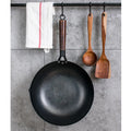 Handmade traditional black iron wok with a long wooden handle on a kitchen counter.