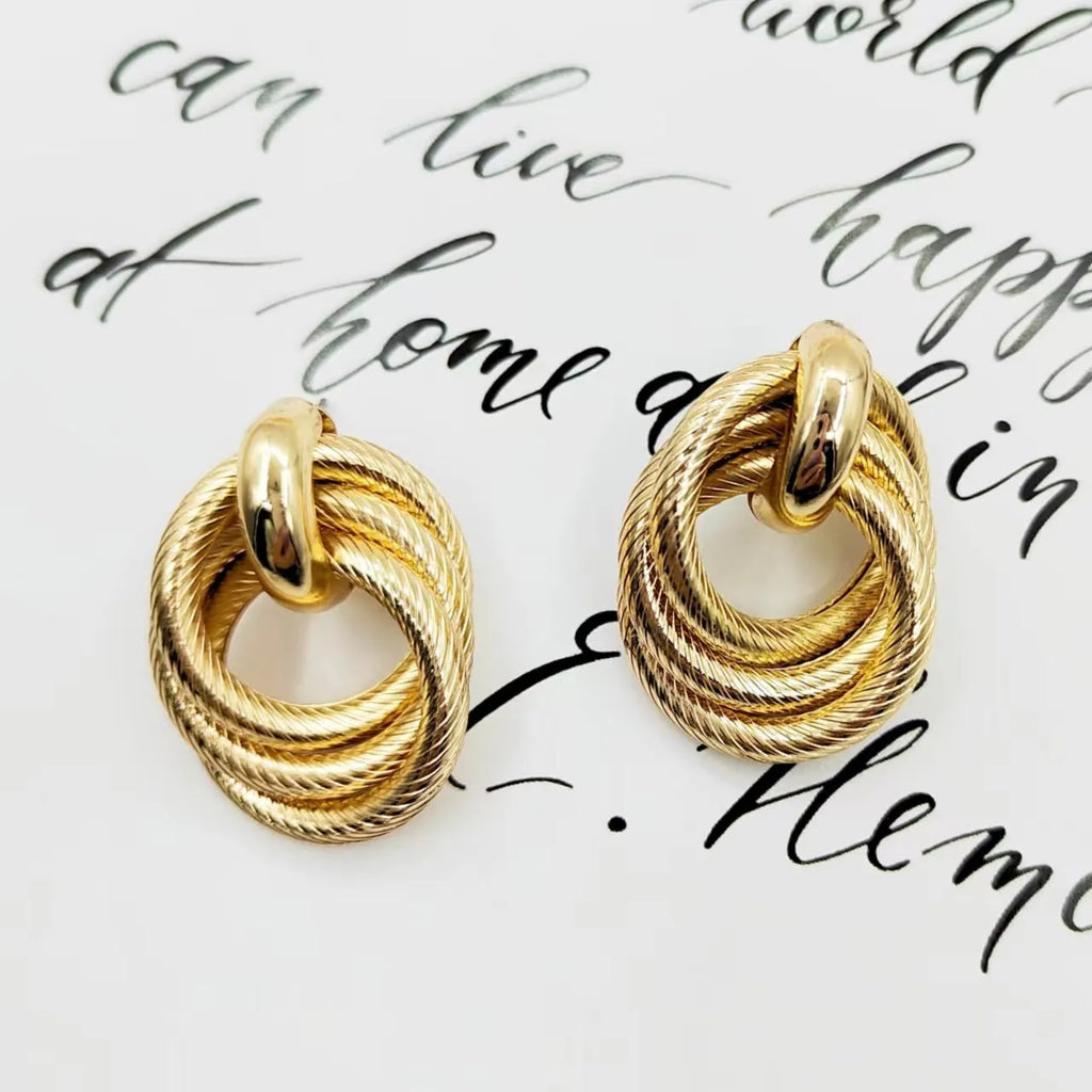 Geometric ring embossed twisted metal stud earrings in gold colour on a plain background