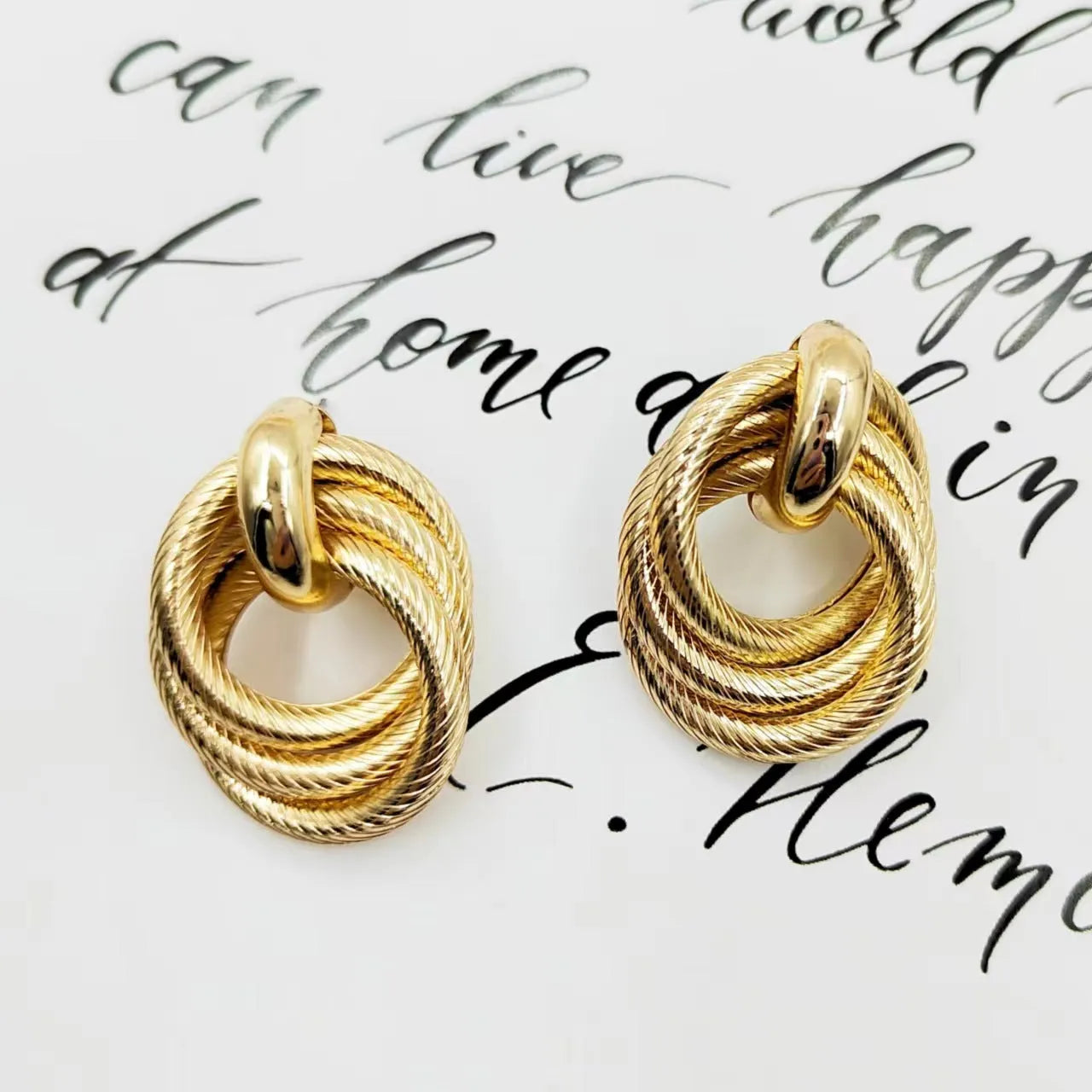 Geometric ring embossed twisted metal stud earrings in gold colour on a plain background