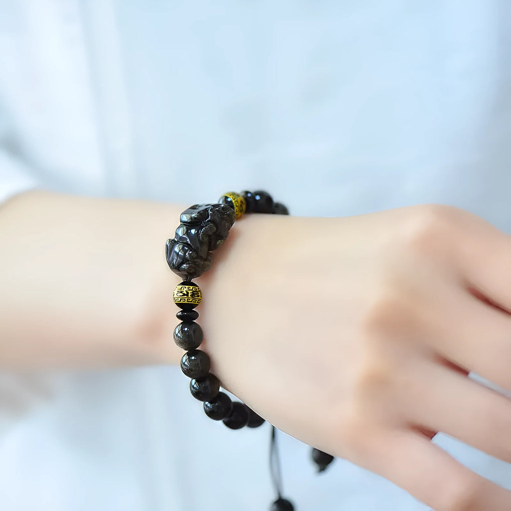 Golden obsidian bead Pi Xiu bracelet with hand-woven design on a wrist.