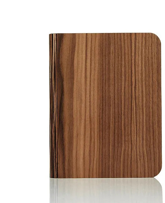 A solid wood adjustable LED book light on a desk next to a book.